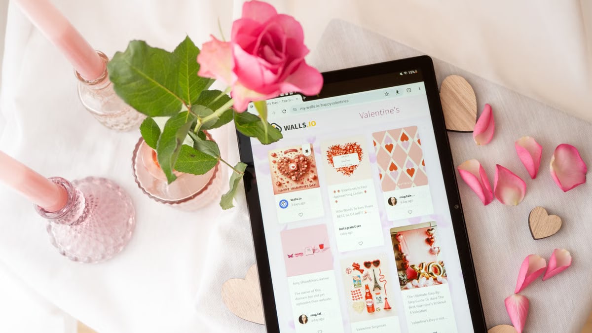 Flat lay of a tablet displaying Valentine's Day content with a pink rose and petals, perfect for romantic themes.